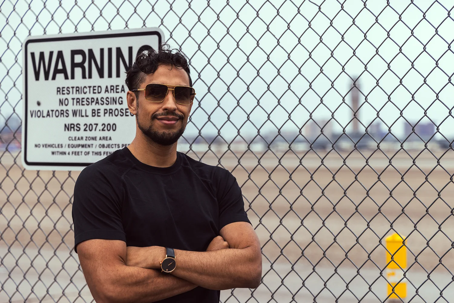 Crypto Grift brand photo, Alex Guerra in sunglasses in front of a restricted-area fence