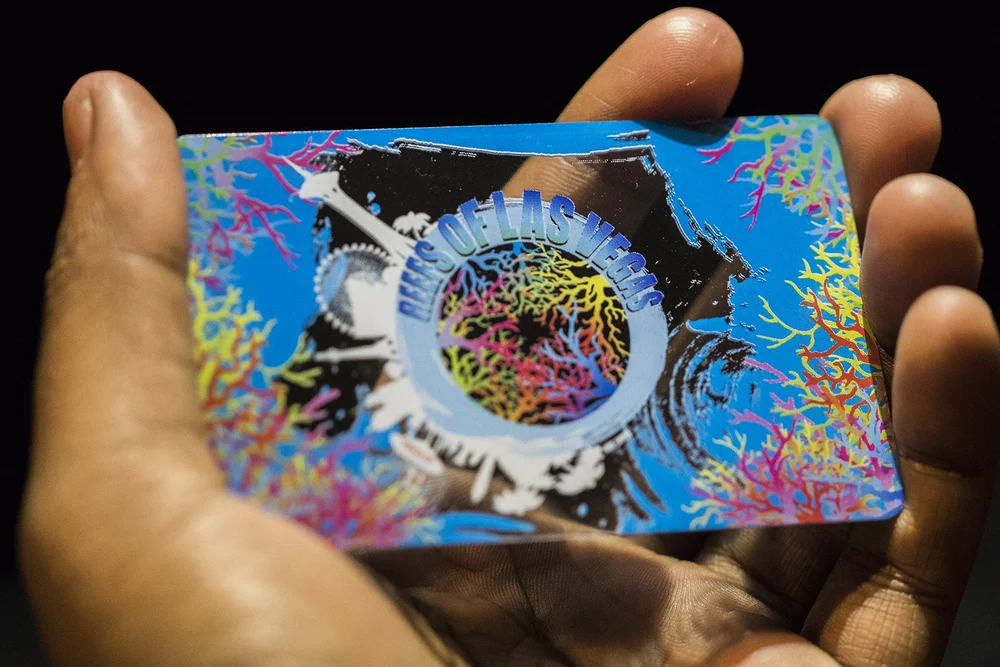 Hand holding a Reefs of Las Vegas VIP membership card, colorful coral globe over the Las Vegas skyline